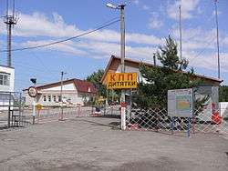 Three small buildings beside a road. The road is blocked with a white and red striped gate and a yellow and red sign reads "KPP Dytyatki" in Ukrainian