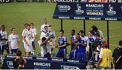 A coloured photograph of the Chelsea squad standing on a podium, celebrating their second Premier League Asia Trophy win.