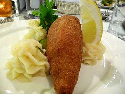 A chicken Kiev on a plate served with mashed potato and a lemon wedge