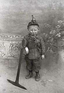 A child holding a pickaxe with a pipe in his mouth