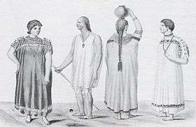 Two men and two women. The men wear necklaces with crosses around their necks. One of the women wears a necklace the other shown from the back has braided hair. Three of them wear wide robes, the third wears a shirt and kneelength trousers.