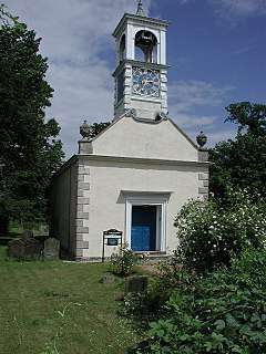 The simple west end of a church with a complex two-stage bellcote containing a clock in the lower stage