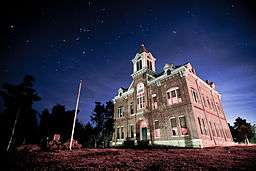 An old, two-story brick courthouse with third-story bell tower under a starry night sky.