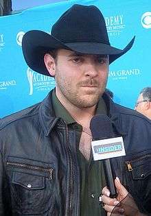 A young man wearing a black cowboy hat and dark jacket