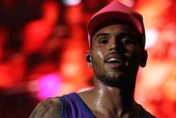 An image of Chris Brown with a pink hat and a blue shirt. He is looking toward the camera.