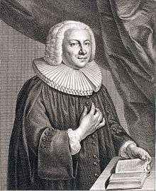 A baroque clergyman in minister's ornate, standing behind a table on which he touches a book with his left hand, while pointing towards his heart with the right hand