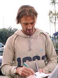 Unshaven white man with scruffy hair wearing a casual hooded top signs autographs