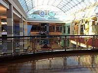 A two-story concourse of a largely abandoned shopping mall, as seen from the upper level. Present is a sign reading "Neighborhood A, Neighborhood C, Food Court".
