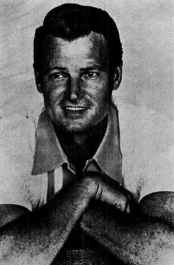 A dark-haired man wearing a casual shirt, with his arms folded in front of him
