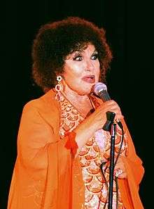 A woman wearing an orange dress and earrings, holding a microphone
