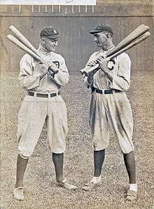 Two batters holding bats, conversing.