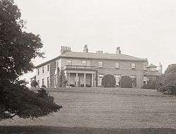 Black-and-white photograph of a mansion in parkland, with a portico on the left-hand side of the façade