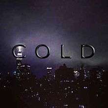 Black, shining text displaying the word "Cold" in front of a city during nighttime with grey clouds and lit buildings
