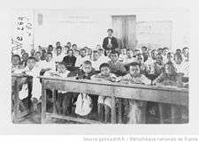 Children tightly packed on benches at desks in a crowded classroom