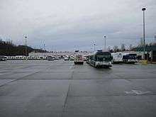 A large, paved parking lot with buses parked in rows