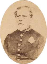 Sepia toned tintype photograph half-length portrait of an older, bearded man wearing a simple military frock coat with large buttons and a single medal over the left breast
