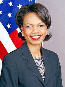 Condoleezza Rice wearing a dark blue jacket over a patterned blouse. The United States flag is in the background.
