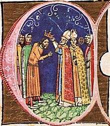 A bishop puts a crown on the head of a bearded man.
