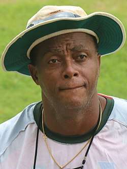 A young black man, in a baseball cap, looking ahead, in a black training top