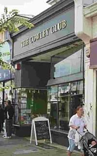 A store front painted grey. At the top of the building is "The Cowley Club" in raised Times Roman font.