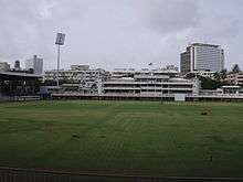 Brabourne Stadium in Mumbai. Image shows the playing field, part of west stand and the art-deco pavilion. Floodlight tower stands next to pavilion on the left.