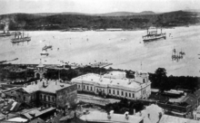 Photograph of ships in a bay, with buildings in the foreground