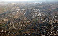 Cumbernauld from the air with St. Maurice's Pond at the bottom and Longannet Power Station on the far side of the Forth at the top. To the left the Forth and Clyde Canal and to the right Fannyside Lochs can be seen.