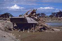 Image showing a mangled bridge split across a river with wood debris piled up against a section of the bridge.