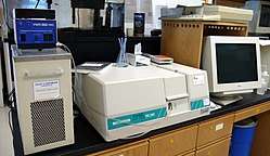 Photograph of a UV-vis spetrophotometer consisting of two white boxes and a computer monitor on a desk