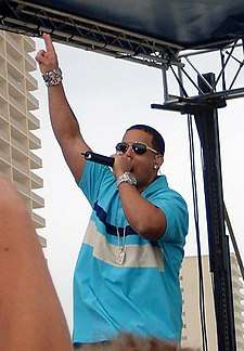 Daddy Yankee wearing sunglasses and holding a microphone.