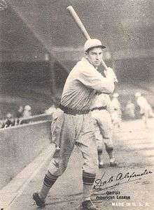 A man wearing a baseball cap and jersey poses prior to swinging his baseball bat.