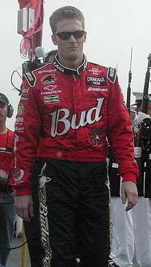 A man in his late twenties wearing sunglasses and red racing overalls