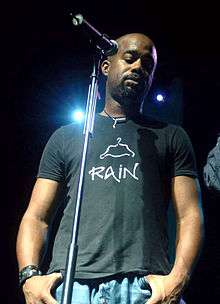 A dark-skinned man in a t-shirt and jeans standing at a microphone