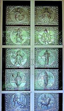 A silver door with ten panels in two columns. The panels depict from top left clockwise a lion-faced man, a man with a bow and axe, a man with a bow, a man playing a flute, a man on a horse, a man with one of his feet on the head of a kneeling man, an arms-akimbo man, a boar-faced man, a man whose body below the waist is a tortoise and a man whose body below the waist is a fish.