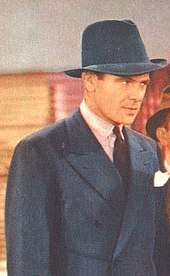 Color photo of a man wearing a blue suit and hat.