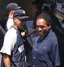 A man in a navy blue and grey windbreaker with the word "New" visible stands on the left facing a man in a navy blue polo shirt who is looking up at the camera.