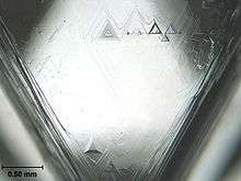 A triangular facet of a crystal having triangular etch pits with the largest having a base length of about 0.2 millimetres (0.0079&nbsp;in)