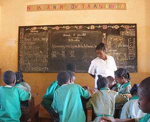 Malagasy children in green school uniforms working in groups as a teacher in white looks on