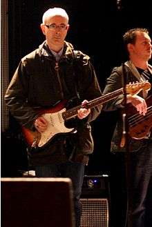 Dik Evans holding a guitar in front of a microphone stand