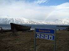 View of the Djúpavík village sign and the wreck of the Suðurland freight ship with Ingólfsfjörður in the background.