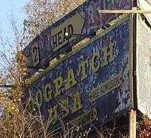 A billboard with peeling paint and faded yellow lettering that reads Dogpatch, USA: free admission.