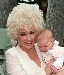 A woman with blonde curly hair holding a baby