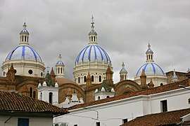 Roofs and towers of a small white church and a larger brown brick church with three large white-blue cuppolas.