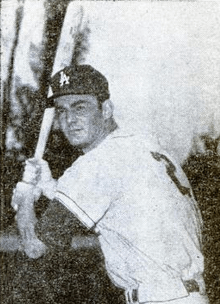 A man in a white baseball jersey with a block "2" on the reverse and dark cap with an interlocked white "LA" on the face holds a baseball bat over his right shoulder