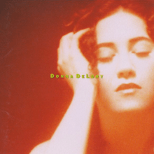 A photo of de Lory in red and orange hue, along with the title of the album in a bright yellow font appearing across her hand and part of her face.