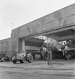 Twin-engined transport aircraft being towed from hangar by a tractor