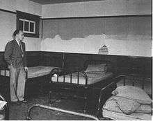 A black and white image of Dr. Le Vann in the Michener Centre, before a number of empty patient beds.