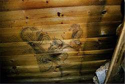  A wooden planked wall on which can be seen a stylised drawing of a woman's head and other ornamental shapes and objects