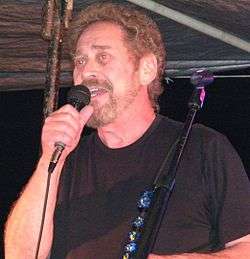 A man with curly light brown hair and a beard singing into a microphone