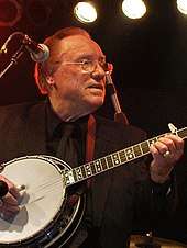 An older man wearing a dark suit and playing a banjo